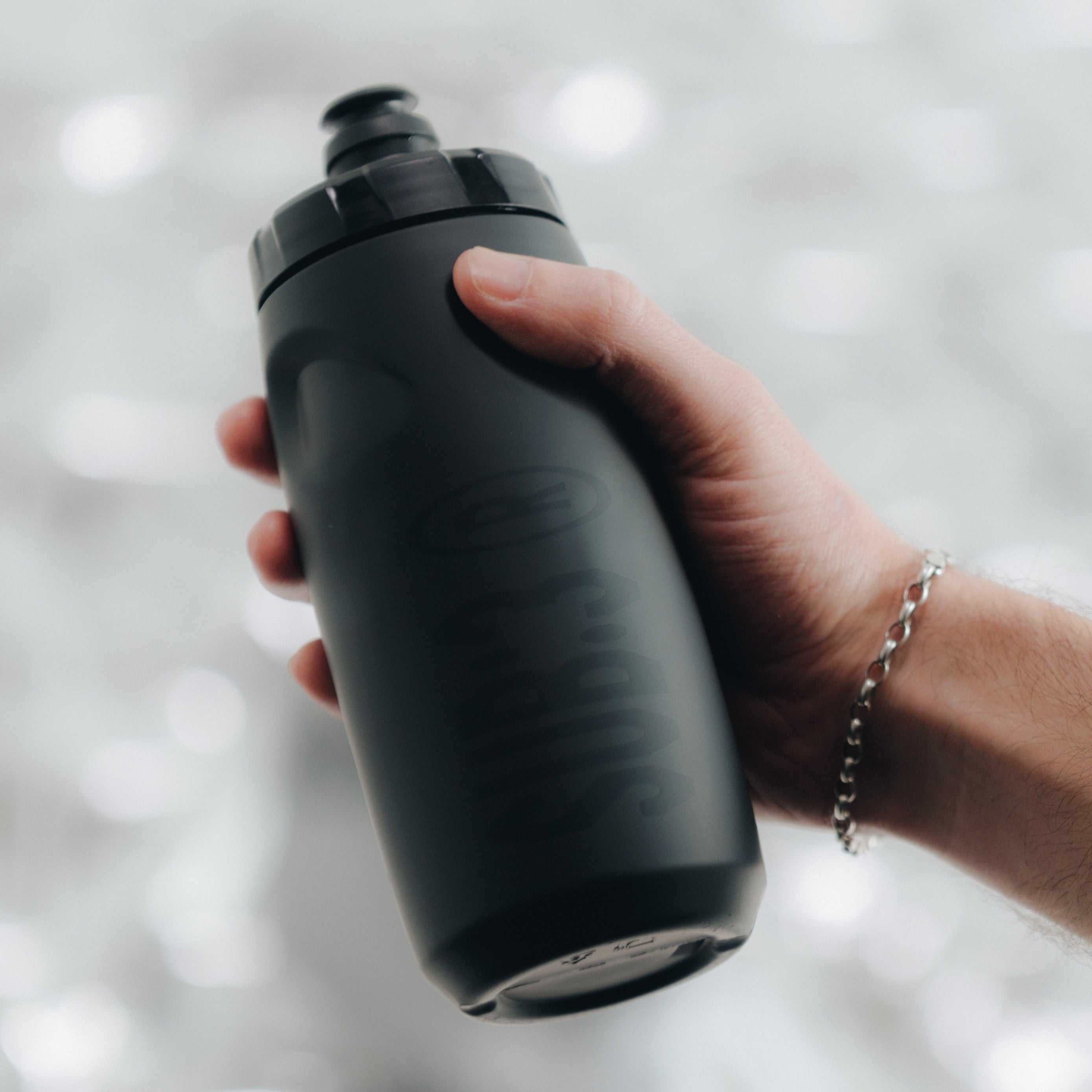 Person holding a black water bottle against a blurred natural background