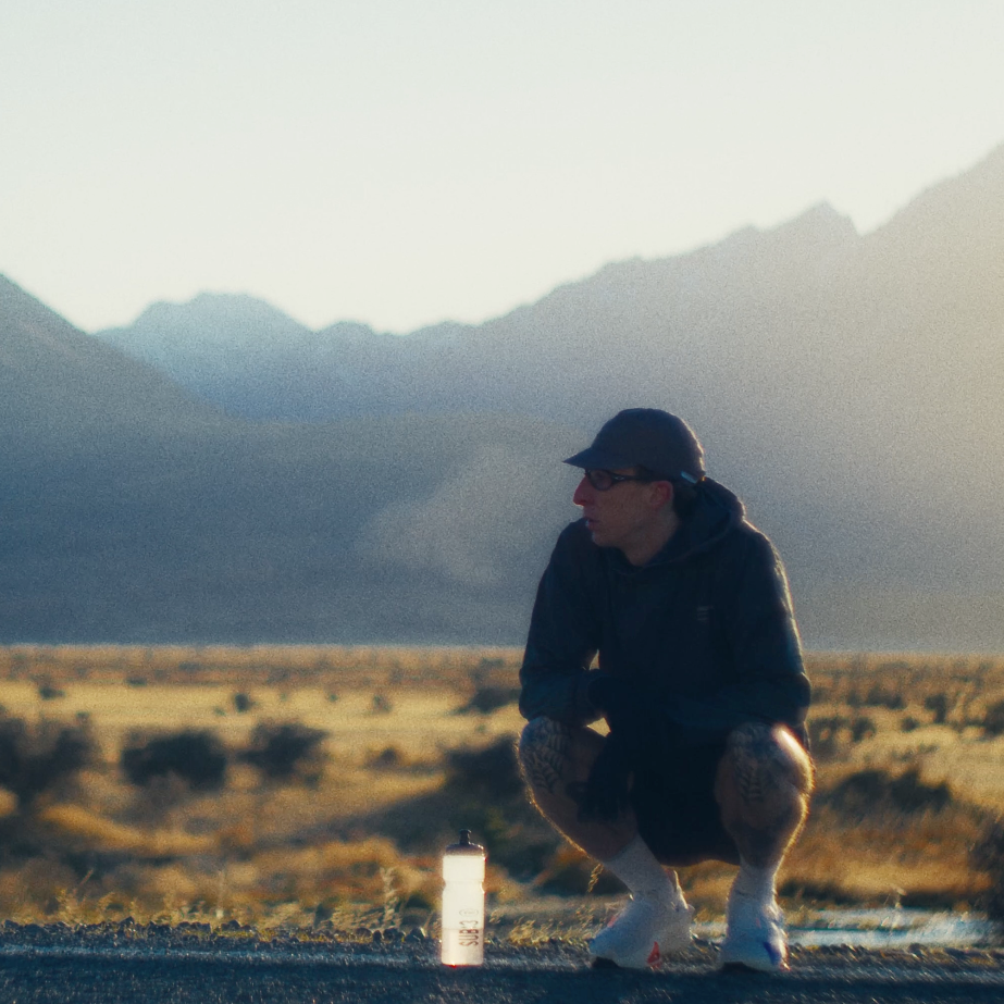 Person squatting in a desert landscape with mountains in the background